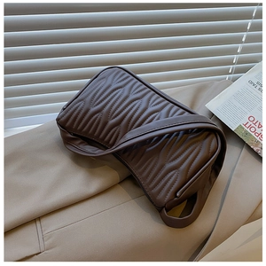 Detailed close-up of dark brown wrinkled leather texture and wide strap on an underarm bag