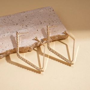 Macro detail of geometric gold earrings with sparkling crystals on stone background