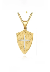 Close-up of golden hammer textured shield pendant with silver cross detail on white background