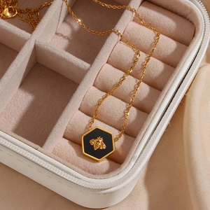 Detail of a hexagonal gold bee pendant necklace displayed on a beige jewelry box with silk