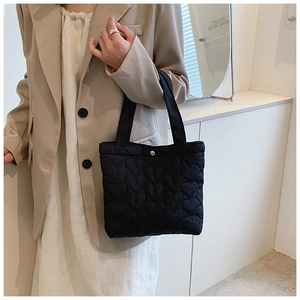 Detail of black tote bag featuring heart quilted texture held by a fashion model