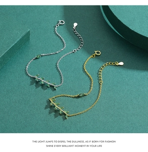 Detail of silver and gold leaf bracelets with green stones on a luxury textured background