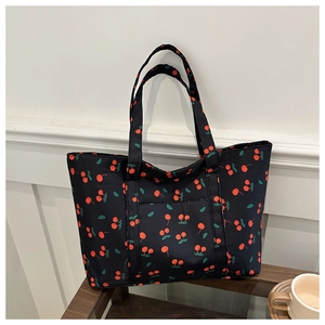 Detailed view of black tote bag with red cherry print on dark wood table