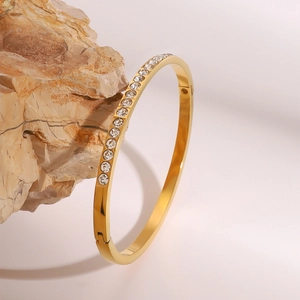Detail of gold stainless steel bangle with crystal inlay on a textured stone prop