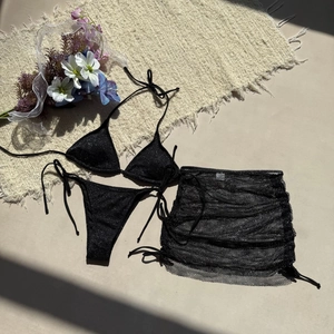 Détail à plat d'un bikini noir scintillant avec jupe de plage en maille transparente
