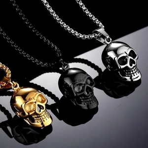 Three oversized skull necklaces in gold, black, and silver with box chains on black reflective surface