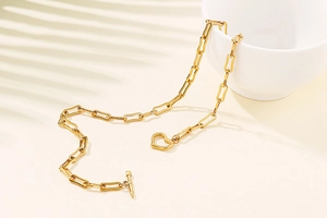 Detailed view of golden paperclip chain necklace with heart pendant and OT toggle clasp