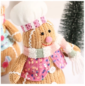 Close-up of a gingerbread man plush toy with pink sequin vest and knit chef hat