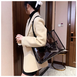 Detail of a dark grey transparent PVC tote bag worn by a model in a modern office style