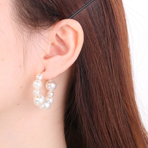 Detailed view of U-shaped stainless steel earrings with white pearls on a model