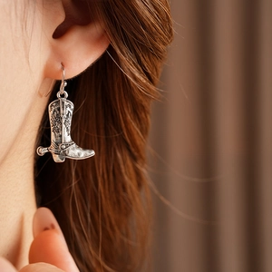 Détail de boucles d'oreilles bottes de cowboy argentées vintage ciselées sur un modèle
