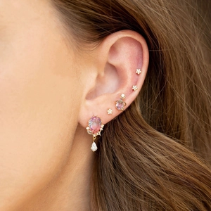Close-up of elegant gold flower studs and pink teardrop gemstone earrings on model