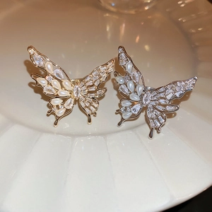Detail of gold and silver butterfly rings with pearls and zircons on a white plate