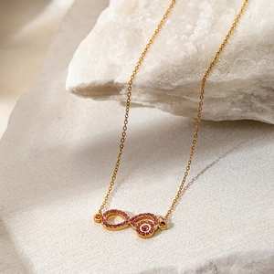 Macro view of gold infinity necklace with pavé pink zircon stones on white rock