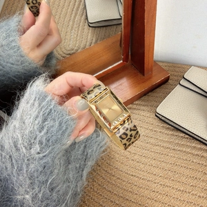 Detail of a rectangular gold watch with leopard print strap held in hand for lifestyle view