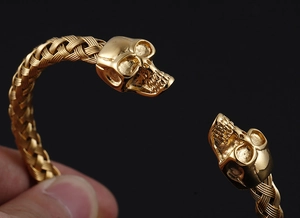 Close-up of golden woven stainless steel bracelet with detailed skull heads on ends
