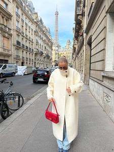 Detailed view of an ivory long wool coat paired with a chic red embossed handbag