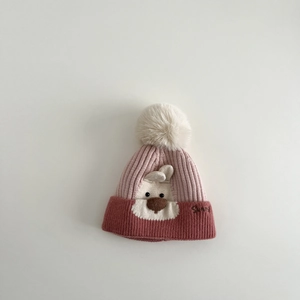 Detail of pink knitted baby hat featuring a bunny design and white faux fur pompom