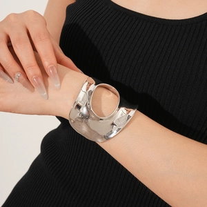 Gros plan d'un bracelet manchette argenté ajouré porté avec un haut en tricot noir