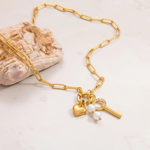Close-up of golden paperclip chain necklace with heart, pearl, and key charms