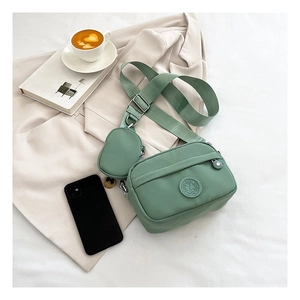 Detail of water-resistant green nylon crossbody bag with mini pouch on beige fabric