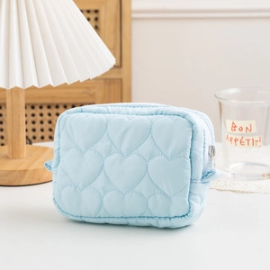 Detail of light blue quilted makeup bag with heart pattern and smooth zipper closure