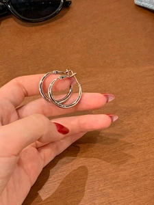 Close-up of minimalist silver hoop earrings held by hand over a wooden background