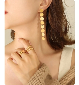 Detail of gold disc drop earrings and textured stacking rings on a female model