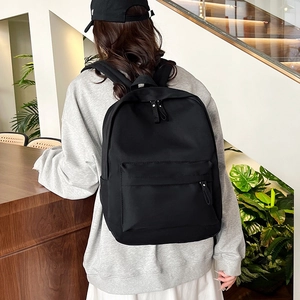 Minimalist black large capacity backpack shown on a model in a modern indoor setting