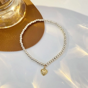 Minimalist silver beaded bracelet with a gold heart pendant on a premium leather mat