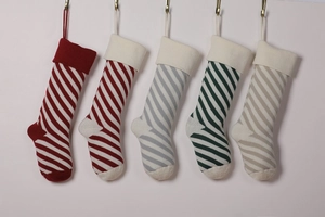 Row of five knitted Christmas stockings with red, green and grey stripes on white backdrop