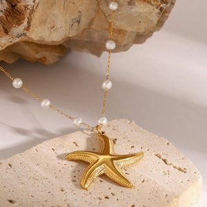 Gros plan du pendentif étoile de mer doré avec perles blanches sur fond de pierre