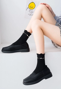 Close-up of black crew socks with pearl accents and ruffled edges worn with leather shoes