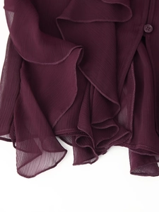 Dettaglio delle balze a strati e del bottone su una camicetta in chiffon viola scuro