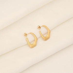 Close-up of golden irregular geometric hoop earrings on soft beige silk background