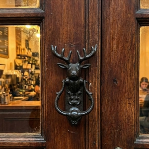 Vintage cast iron deer head door knocker mounted on a rustic solid wood entrance door
