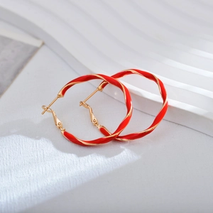 Close-up of red and gold twisted metal hoop earrings on a white textured surface