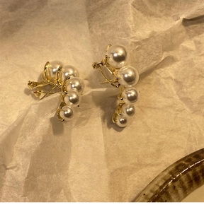 Detailaufnahme eleganter goldener Ohrklemmen mit fünf weißen Perlen in Bogenform