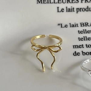 Minimalist golden bow open ring on elegant white ceramic surface with decorative text
