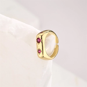 Detail of gold-plated open ring with three sparkling red zircon stones on a white stone