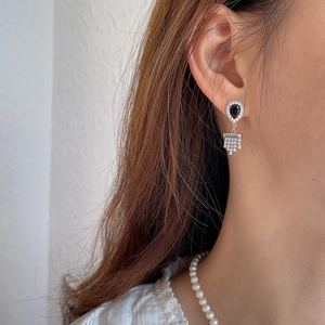 Detail of silver drop earrings with black stones and rhinestone tassels on ear
