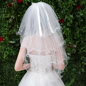 Detail of white bridal veil with pearls, wavy edges and a ribbon bow on green background