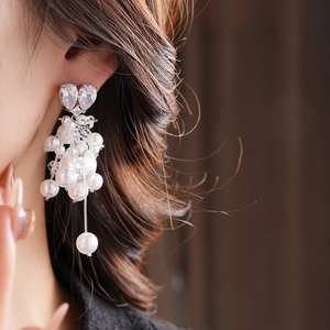 Detail of heart-shaped zircon earrings with long cascading faux pearl tassels on a model