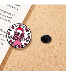 Detailaufnahme der Emaille-Anstecknadel mit rosa Schleife und Blumen auf einer Korkfläche