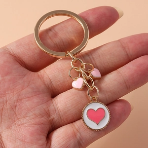 Close-up of gold keychain with white and pink enamel heart charms held in hand