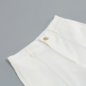 Detail of white trousers showing gold button and sharp crease on high-quality fabric