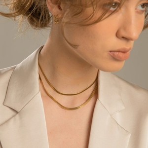 Close-up of double layered gold snake chain necklace on model wearing a beige blazer