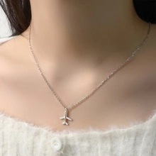 Detailed view of a silver airplane pendant necklace worn on a woman's collarbone
