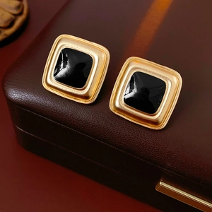 Close-up of vintage square earrings with gold frame and black enamel on leather base