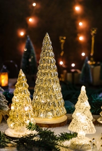 Close-up of glass Christmas trees with LED lights and wooden base on snow surface